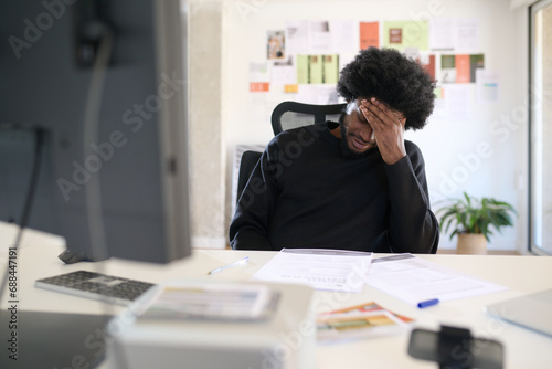 portrait of a creative businessman sitting at his desk with his hand on his forehead exhausted photo