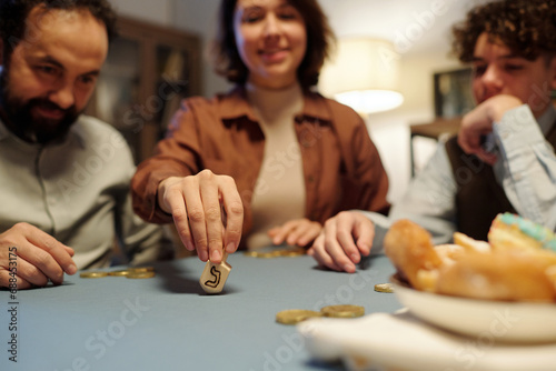 Focus on hand of young woman spinning dreidel with Hebrew letter while sitting by table in front of camera and playing leisure game photo