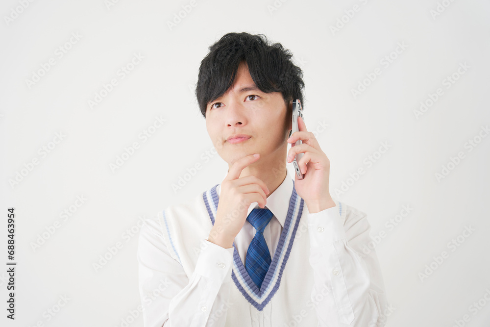 スマートフォンで電話をしながら考える男子高校生　白背景