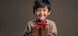 A nice young chinese boy happily surprised with a gift in his hands with a gray background