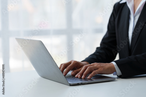 Close up. Asian businessman working with laptop computer at modern office Businessman in black suit working and typing on laptop keyboard Internet online at the desk in the office.