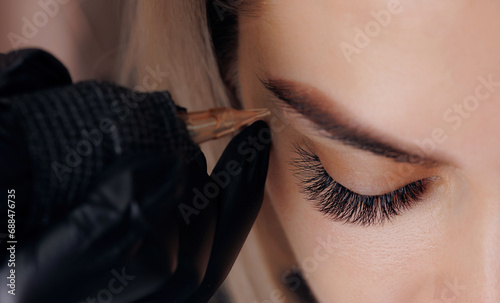 Closeup procedure permanent makeup tattoo for eyebrows of beautiful woman with black brows in beauty salon