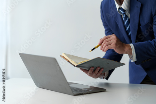 businessman working on laptop computer Print email check work Send information online on white desk Hold a notebook and use a pen to point to business goals that plan success in the office. photo