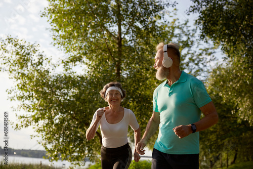 Lovely joyful retirees couple jogging outside in city park in morning