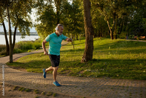 Senior man wearing headset looking at wristwatch running in park