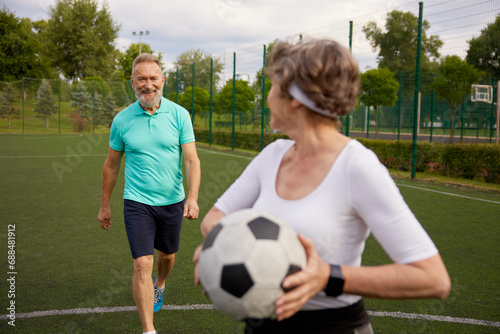 Happy elderly couple with football ball on sportive stadium in city park