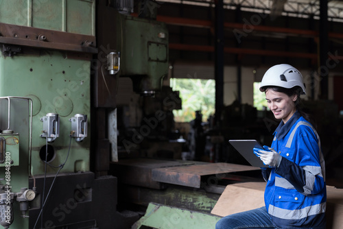 Female engineer working in industry factory, control machine with digital tablet, wearing safety uniform, helmet