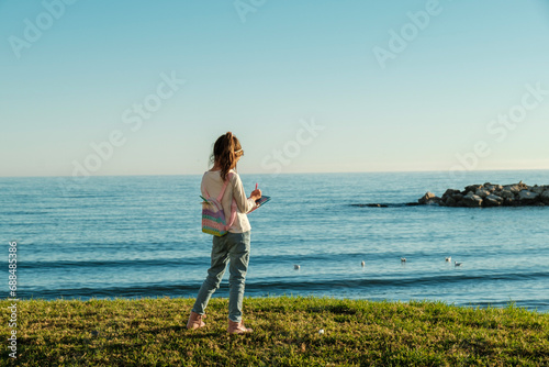 Playa de Pedregalejo, Málaga, niña seis años en el césped, frente al mar, escribiendo en su diario, día soleado, cielo sin nubes photo