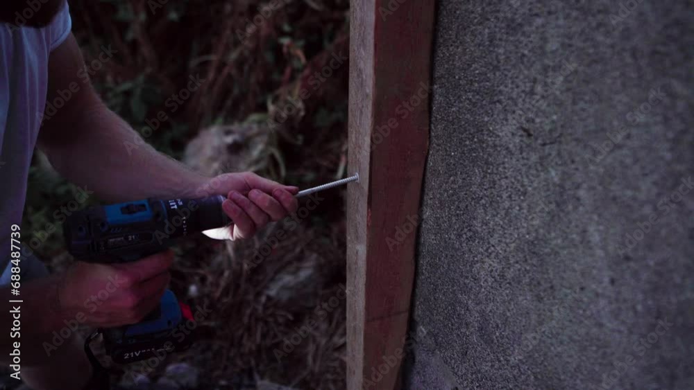 A Man is Using a Drill to Insert a Nail into Wood Intended for the Construction of a Greenhouse in Indre Fosen, Norway  - Close Up