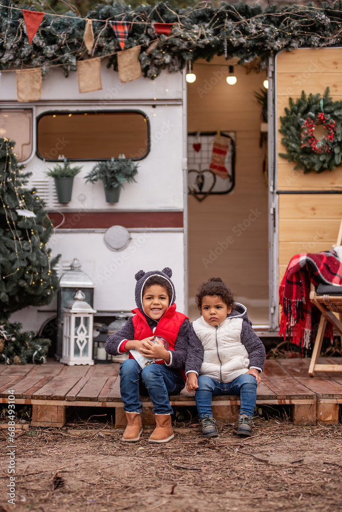 African American boy and girl are sitting on wooden pallets, playing with a Christmas snow globe
