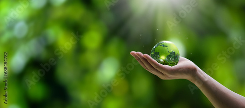 Hand holding crystal globe in green forest. ESG concept for environment, society and governance in sustainable and ethical business. green energy and growth
