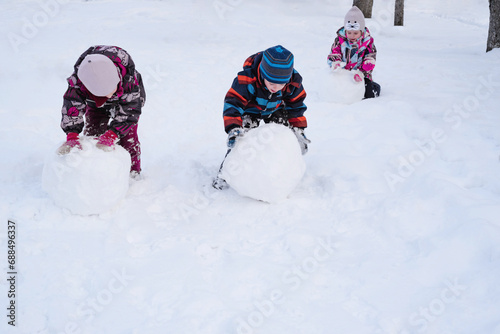 Happy children rolling a snow globe for a snowman. Children playing with snow. Winter entertainment for children. Copy space