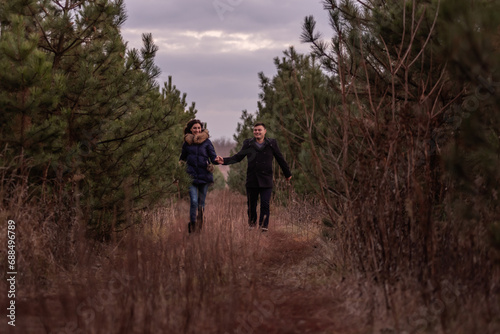 Happy couple running through forest holding hands. Man in coat and a young woman are fooling around