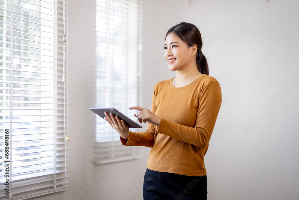 Fototapeta premium Beautiful young concentrated business asian woman wearing shirt using digital tablet while standing in modern workspace