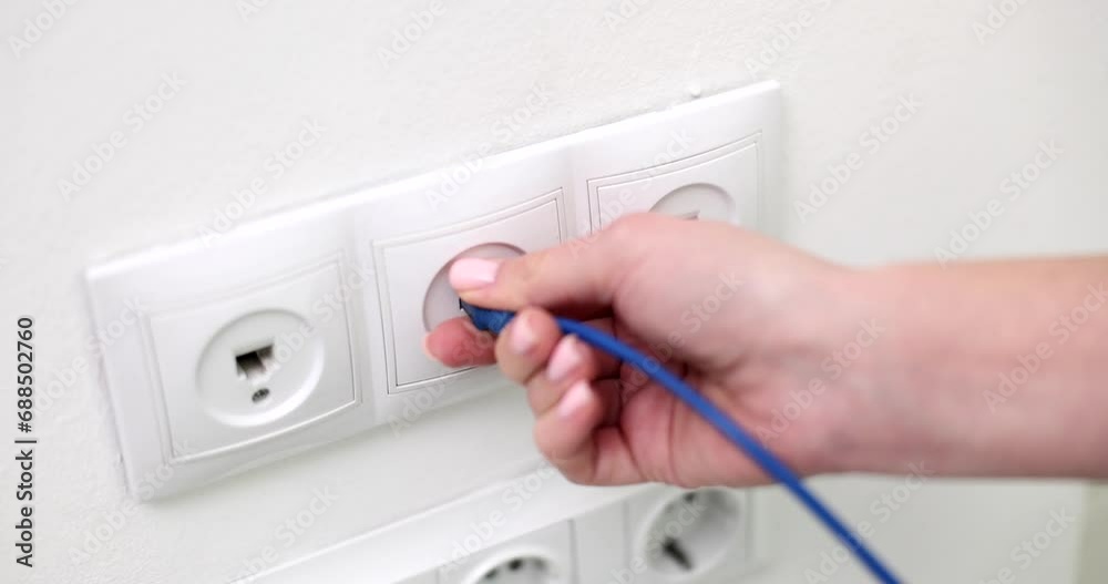 The hand includes the Internet cord in the outlet on the wall, close-up. Wall socket computer The hand includes the Internet cord in the outlet on the wall, close-up. Wall socket computer