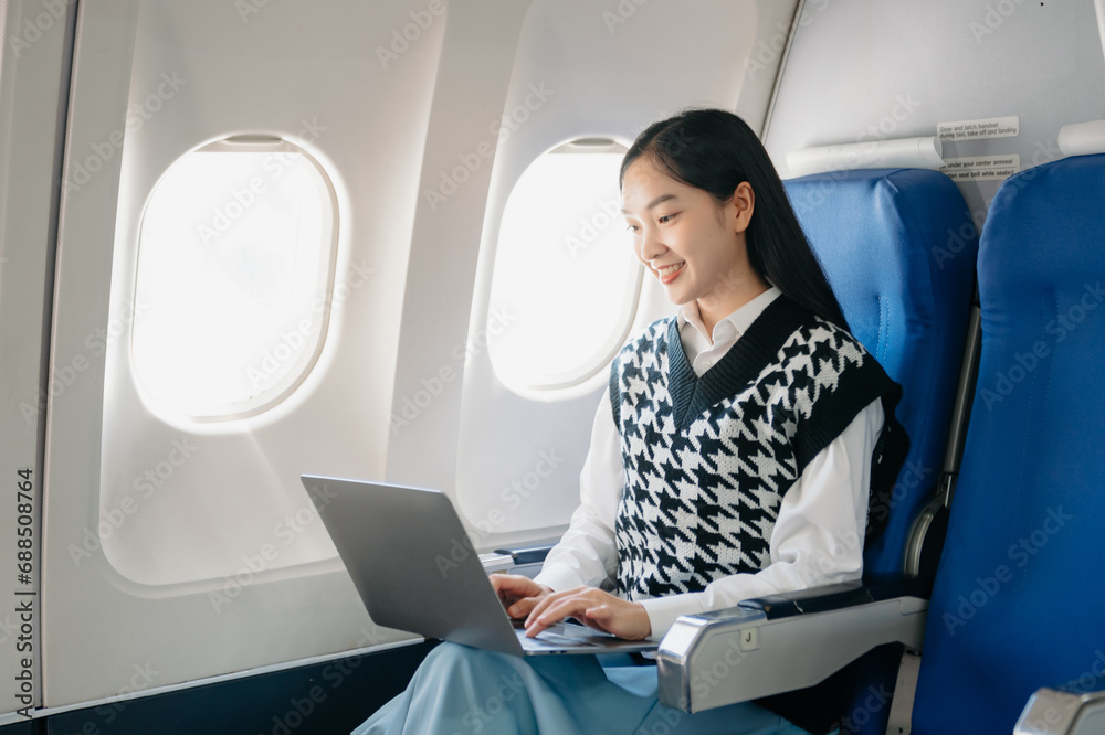 Attractive Asian female passenger of airplane sitting in comfortable seat while working laptop and tablet with mock up area using wireless connection. Attractive Asian female passenger of airplane sitting in comfortable seat while working laptop and tablet with mock up area using wireless connection.