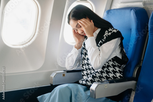 Photo of a frustrated woman sitting on an airplane with her head in her hands. woman sitting in a seat in airplane.
