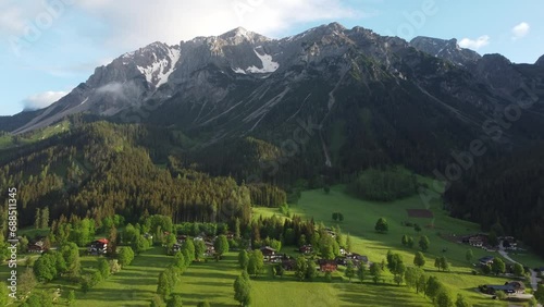 4K drone shot of beautiful misty sunrise at Ramsau am Dachstein, Styria, Austria. Lush green fields and guesthouses at the foot of Dachstein Glacier, popular area for Alpine skiing and snowboarding. photo