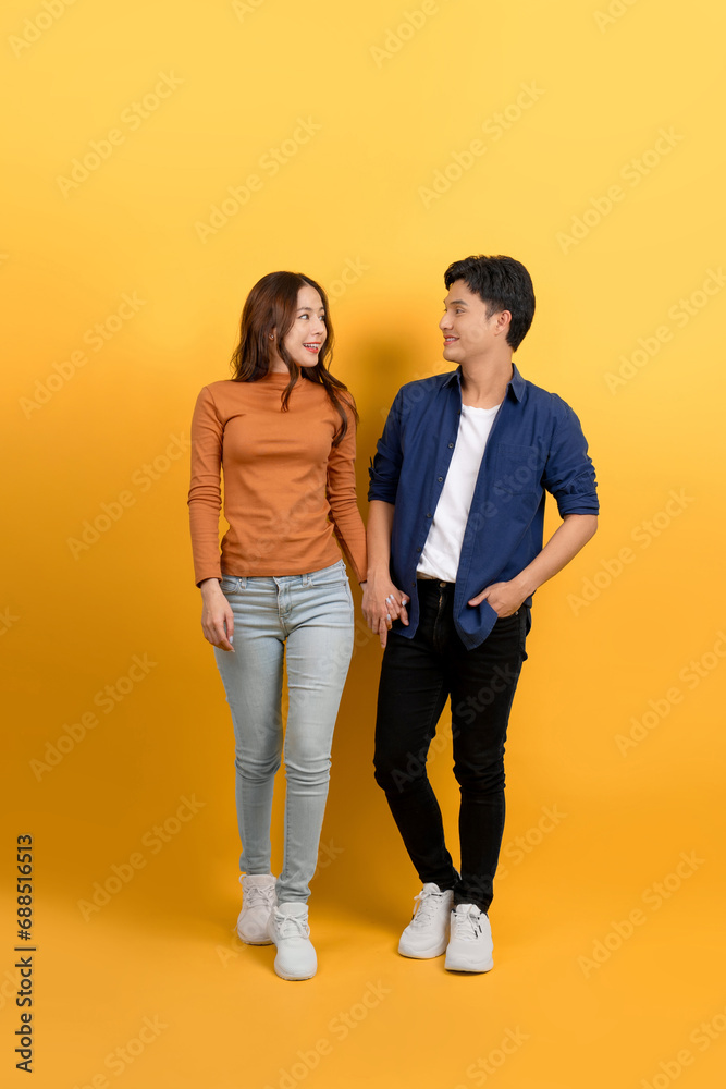 Full view of young Asian couple walking holding hands on blue background.