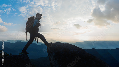 Low angle view of Asian male hikers climbing mountain at sunset rays over the clouds with trekking poles on cliff edge on top of rock mountain, Successful summit concept image. photo