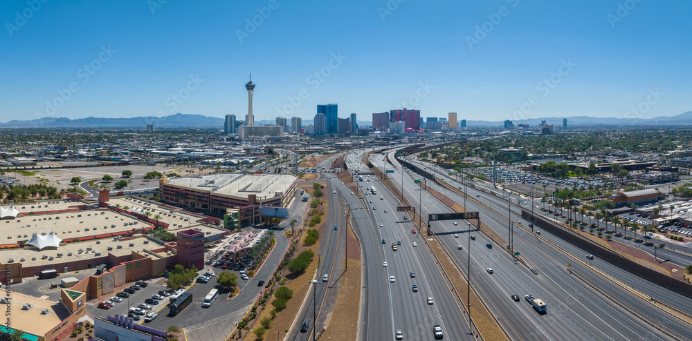 Aerial view of Las Vegas, Nevada, showcasing the Stratosphere Tower, bustling hotels, casinos, clear blue skies, and surrounding mountains during a vibrant midday.