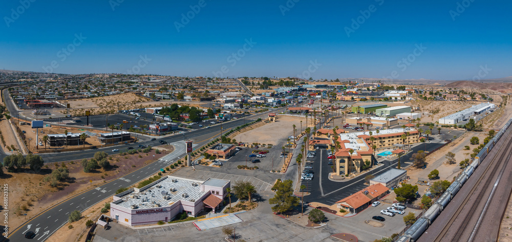 Aerial view of a Barstow U.S. town blending modern and traditional architecture, with earth-toned buildings, red-tiled roofs, and a clear blue sky in a desert setting.