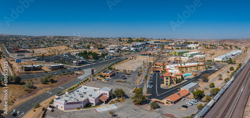 Aerial view of a Barstow U.S. town blending modern and traditional architecture, with earth-toned buildings, red-tiled roofs, and a clear blue sky in a desert setting. photo