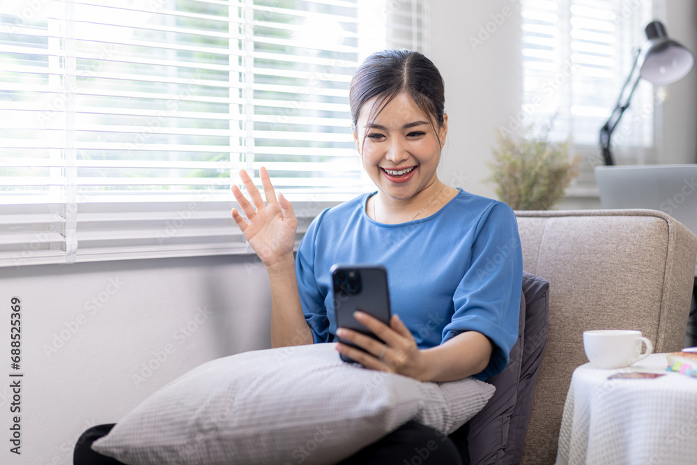 Young Happy Asian woman smiling call video on Phone with fist hand and excited for success on sofa at home. Young Happy Asian woman smiling call video on Phone with fist hand and excited for success on sofa at home.