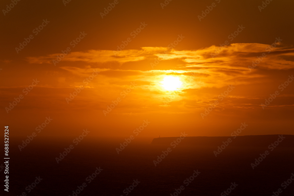 Dramatic Orange Sunset Looming over Seaside Lighthouse
