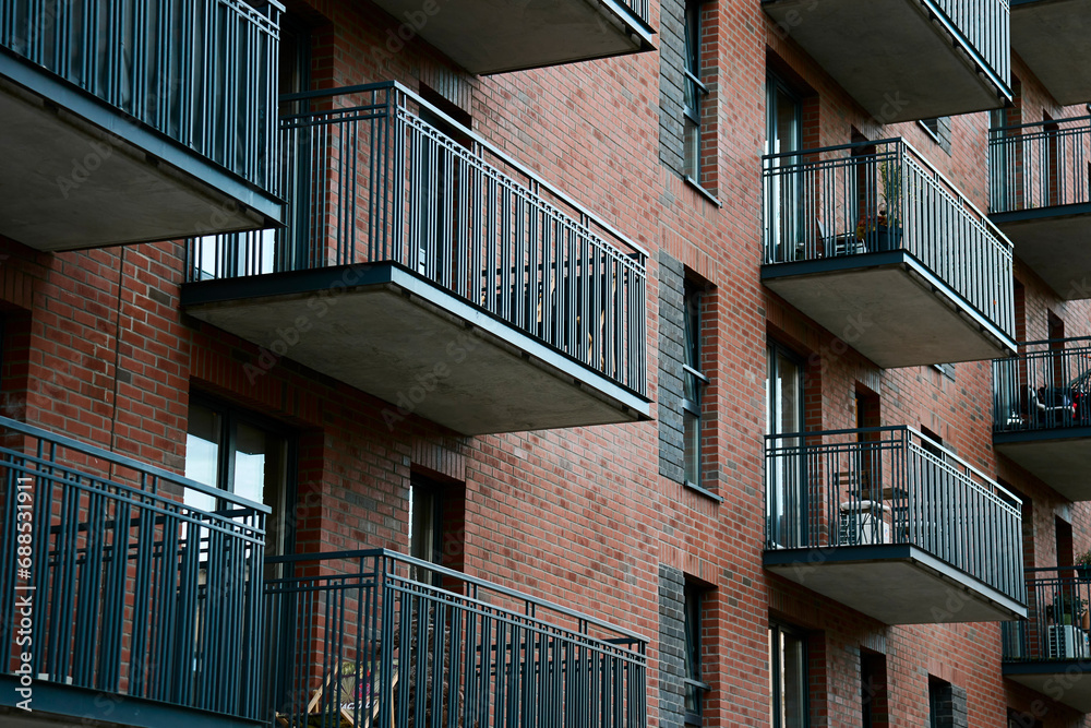 Residential building facade with balconies and windows. Modern city architecture. Apartment building made of red bricks Residential building facade with balconies and windows. Modern city architecture. Apartment building made of red bricks