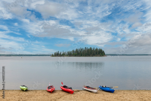 Panoramic view from Elk Island Beach, Alberta, Canada with some canoes on shore over Astotin Lake with one of the tree overgrown islands in water