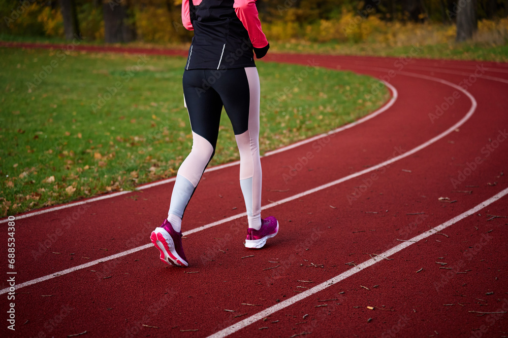 Woman running at track. Female runner jogging at stadium. Active sport exercises at autumn day outdoors. Healthy lifestyle