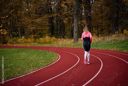 Woman running at track. Female runner jogging at stadium. Active sport exercises at autumn day outdoors. Healthy lifestyle
