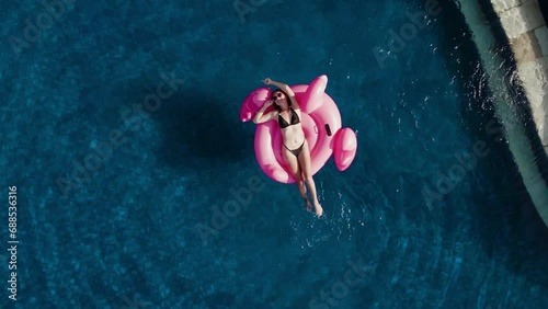 Millennial passion travel blogger in sunglasses swim with inflatable pink flamingo in infinity pool on luxury private villa. Concept of relax rest on summer tropical vacation calm careless aerial view photo