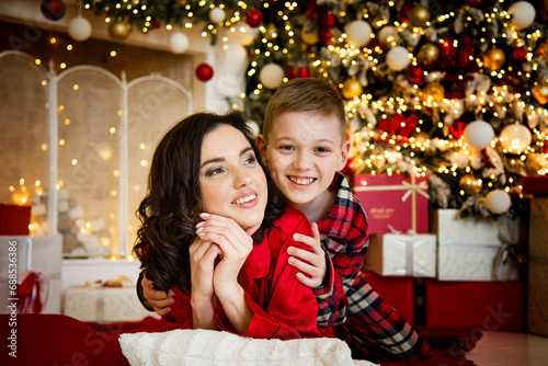 smiling happy mother and son wearing red pajamas posing and hugging near christmas tree in decorated living room