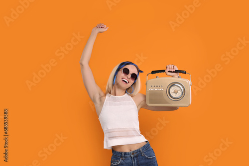 Happy hippie woman with retro radio receiver dancing on orange background photo