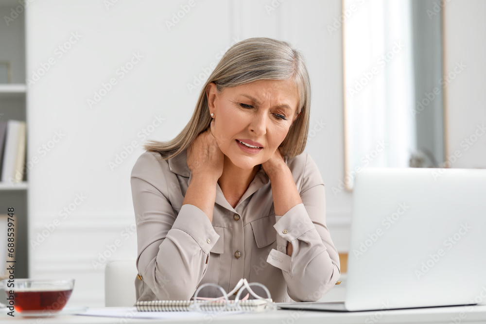 Woman suffering from neck pain at workplace in room