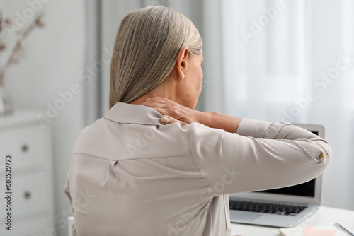 Woman suffering from neck pain at workplace in room photo
