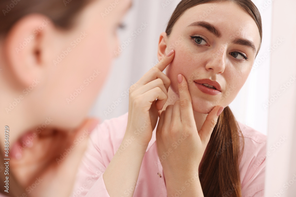 Young woman with skin problem looking at mirror on blurred background