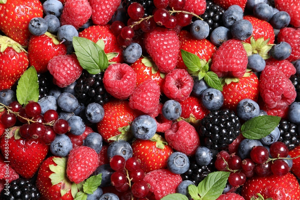 Assortment of fresh ripe berries with green leaves as background, top view