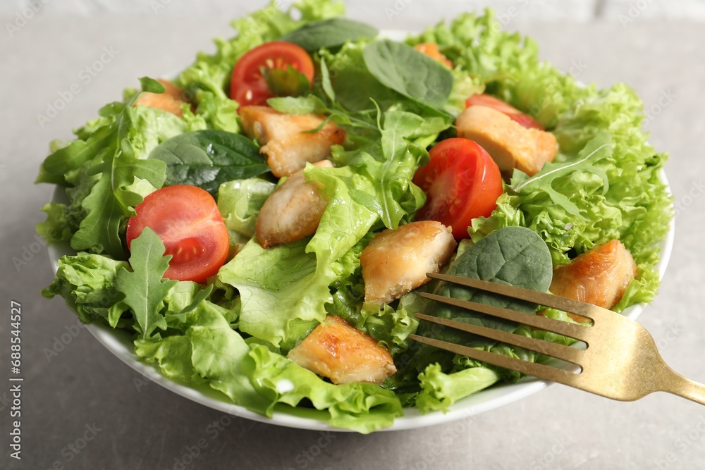 Eating delicious salad with chicken, cherry tomato and spinach at light grey table, closeup Eating delicious salad with chicken, cherry tomato and spinach at light grey table, closeup