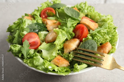 Eating delicious salad with chicken, cherry tomato and spinach at light grey table, closeup