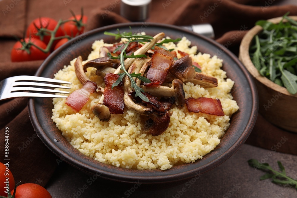 Bowl of tasty couscous with mushrooms, bacon and fork on brown table, closeup Bowl of tasty couscous with mushrooms, bacon and fork on brown table, closeup