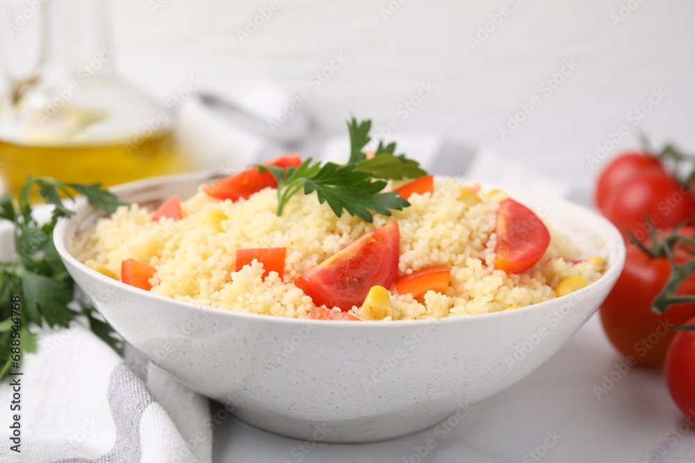 Tasty couscous with parsley, corn and tomatoes in bowl on white table, closeup Tasty couscous with parsley, corn and tomatoes in bowl on white table, closeup