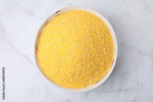 Raw cornmeal in bowl on white marble table, top view