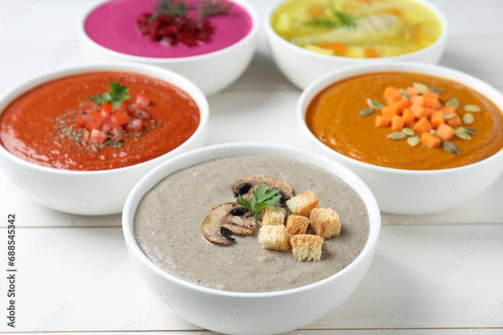 Tasty broth and different cream soups in bowls on white wooden table, closeup Tasty broth and different cream soups in bowls on white wooden table, closeup