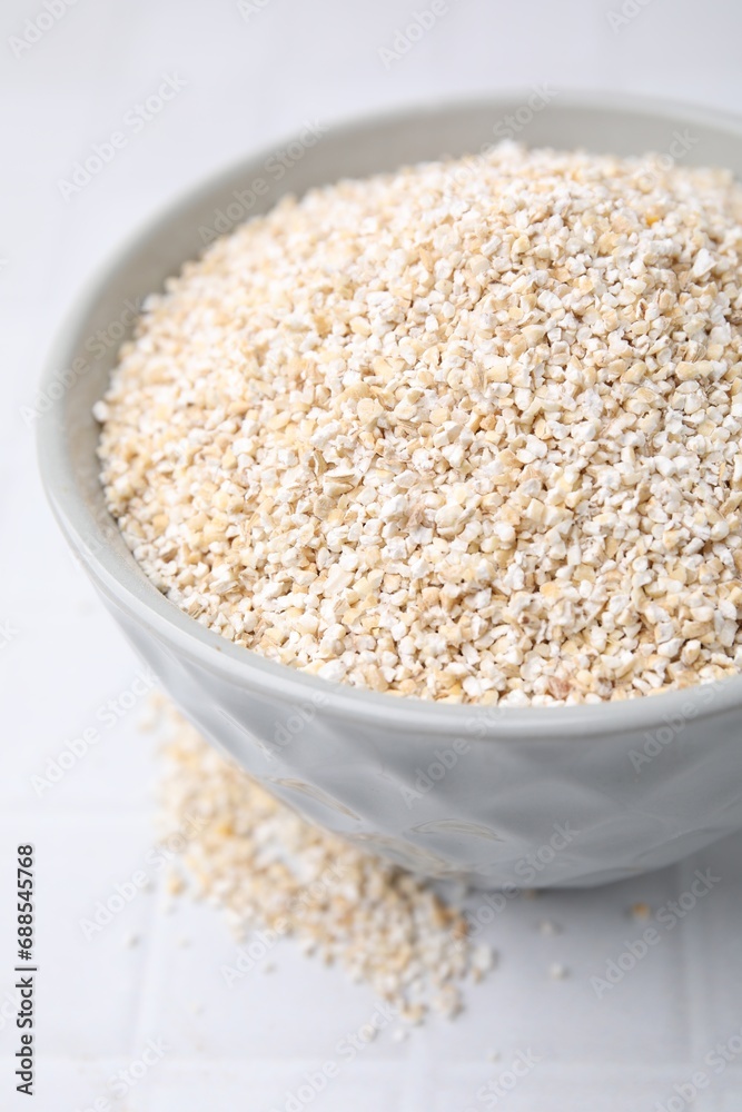 Dry barley groats in bowl on white tiled table, closeup Dry barley groats in bowl on white tiled table, closeup