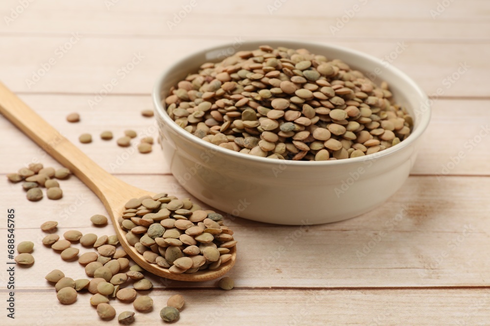 Raw lentils in bowl and spoon on light wooden table, closeup Raw lentils in bowl and spoon on light wooden table, closeup