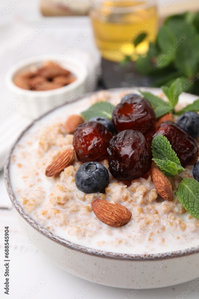 Fototapeta premium Tasty wheat porridge with milk, dates, blueberries and almonds in bowl on table, closeup