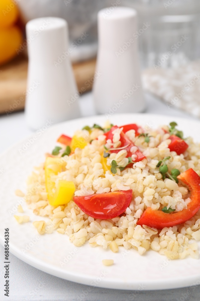 Plate of cooked bulgur with vegetables on white tiled table, closeup Plate of cooked bulgur with vegetables on white tiled table, closeup